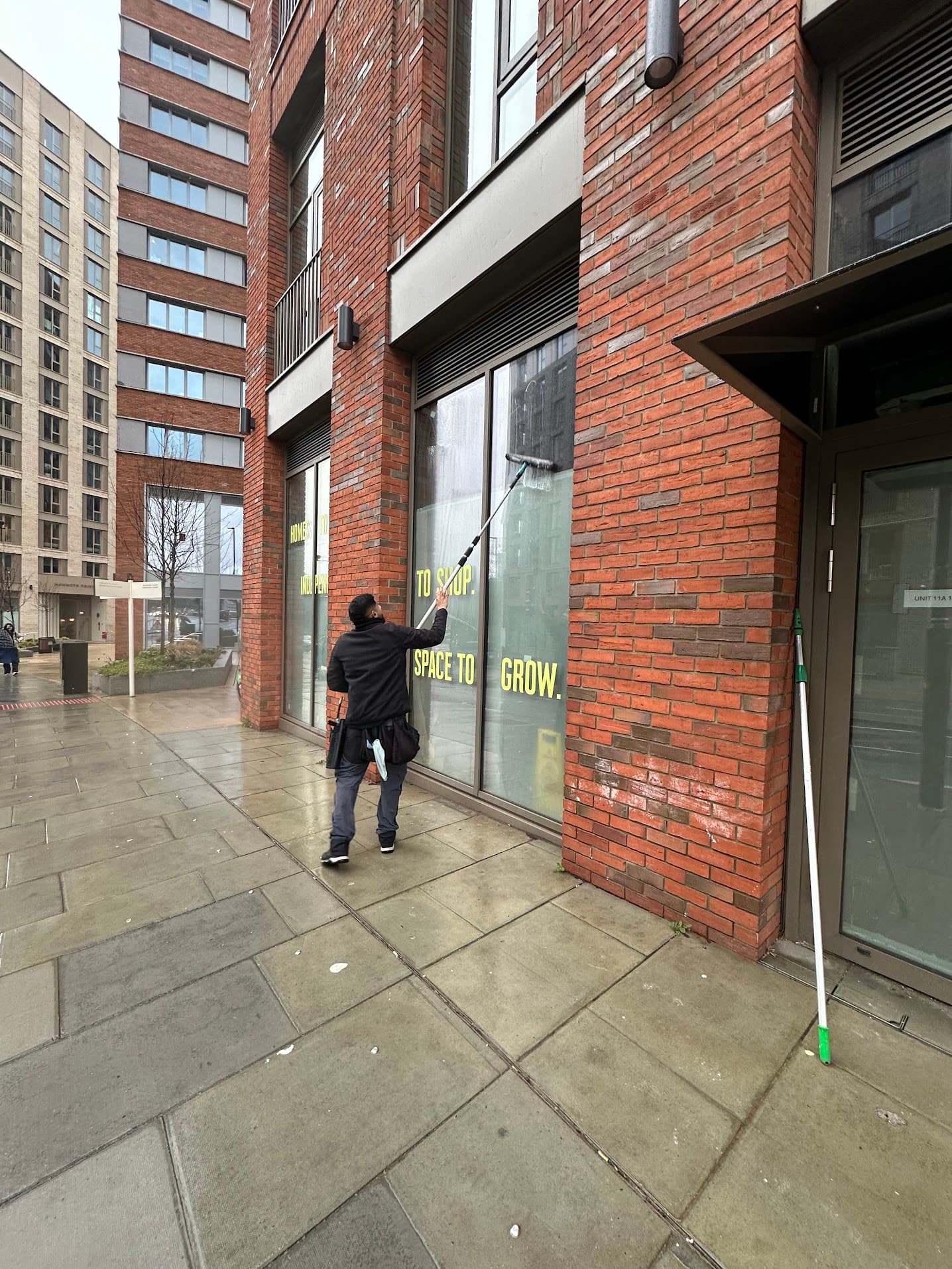Cleaning tall commercial glazing with a water-fed pole at street level.