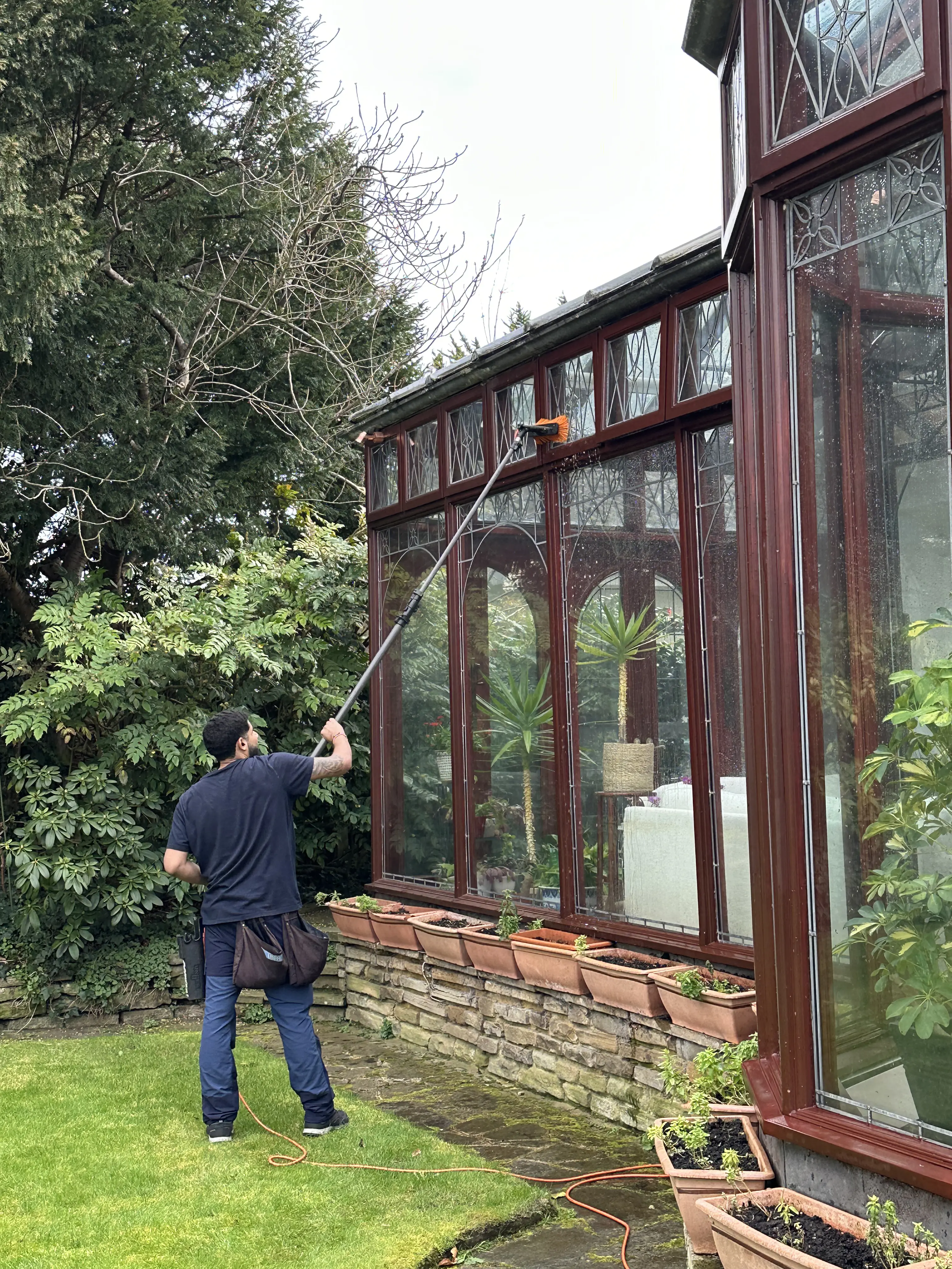 Cleaning large conservatory windows with a water-fed pole from the garden.
