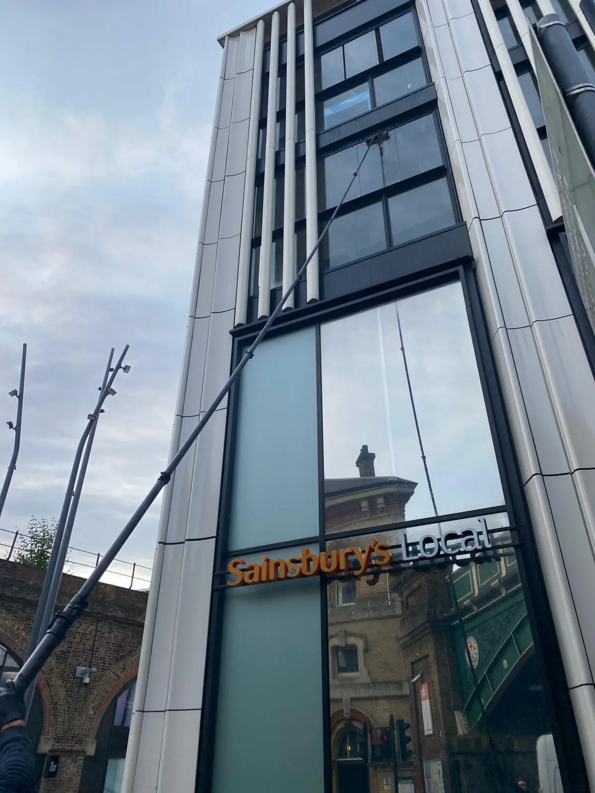 Cleaning high windows above a supermarket storefront with a water-fed pole.