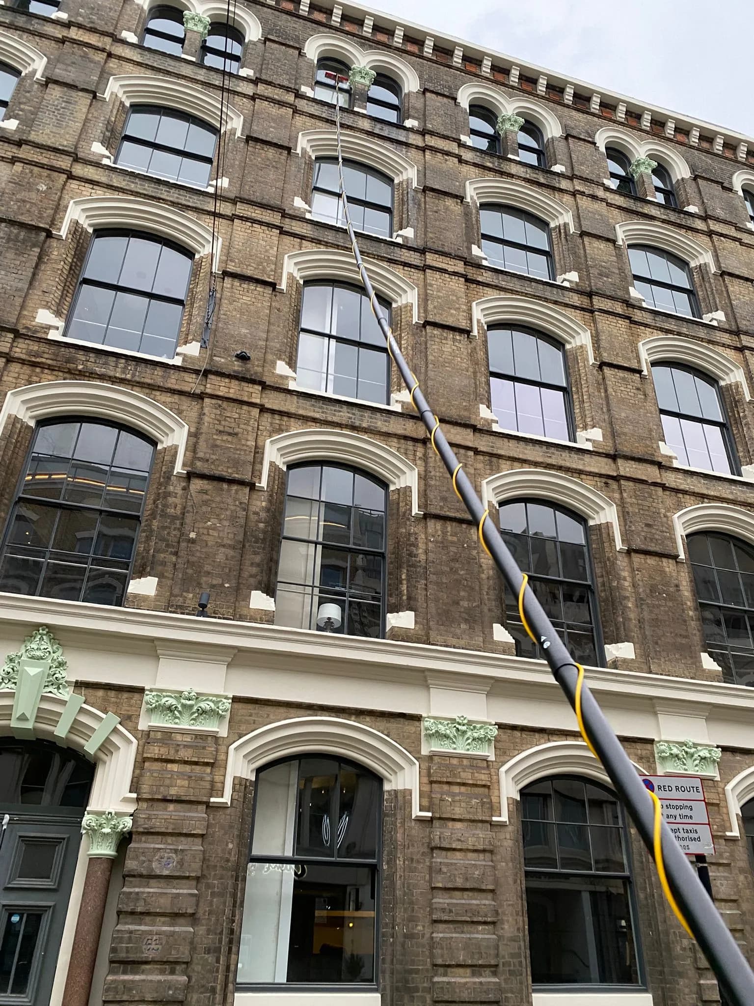 Reaching arched windows several floors up on a brick building with a water-fed pole.