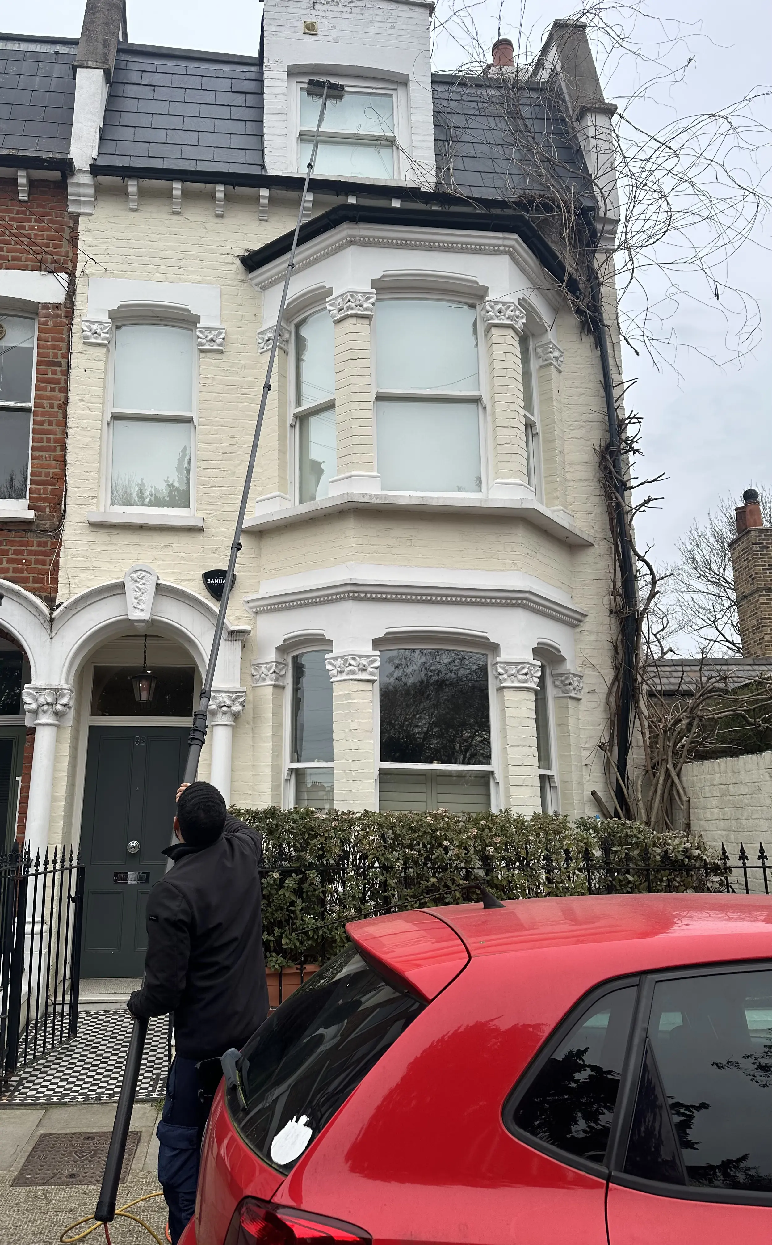 Cleaning sash windows of a Victorian terrace house with a water-fed pole from the street.