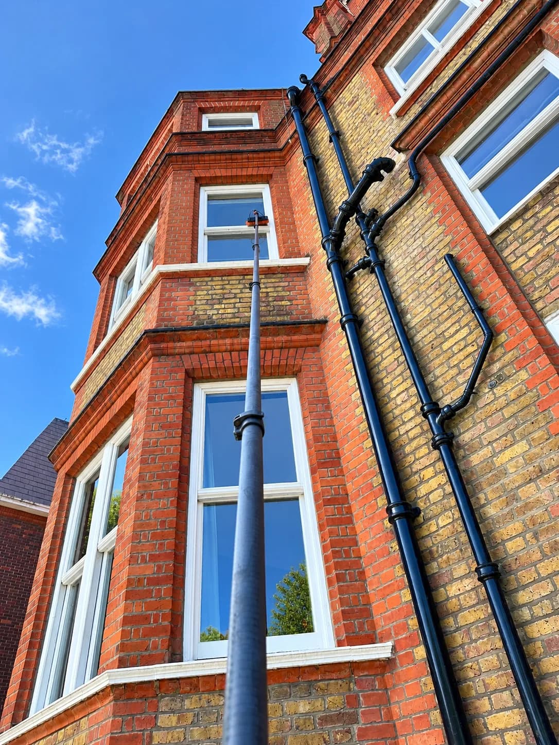 Reaching the upper windows of a red-brick bay-fronted building with a water-fed pole.