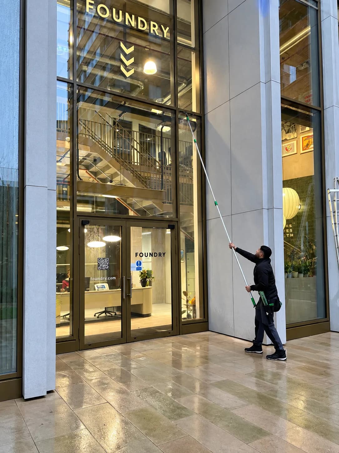 Cleaning the entrance glazing of an office building with a water-fed pole.