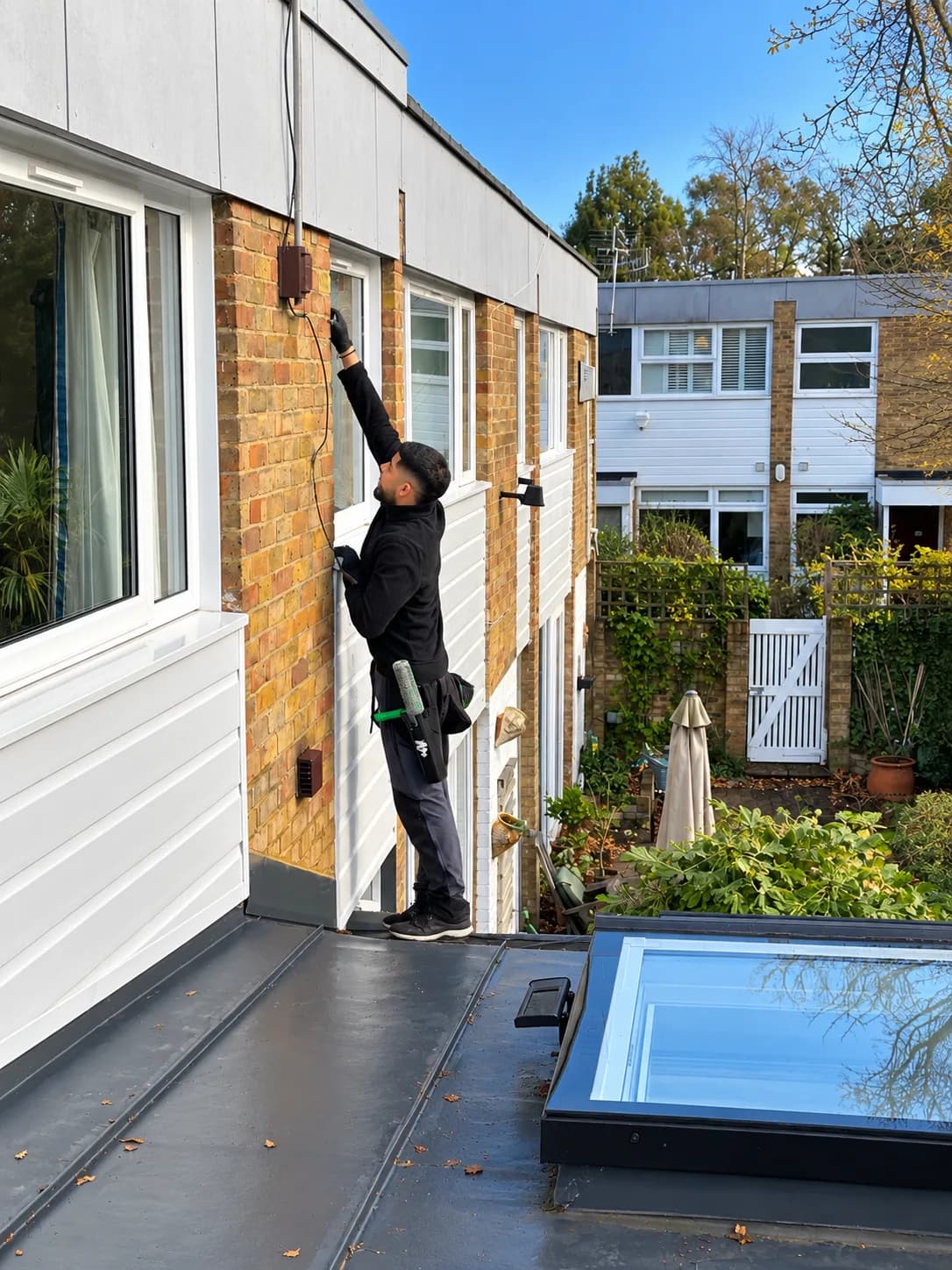 Cleaning upper-floor windows from a flat roof extension, beside a skylight.